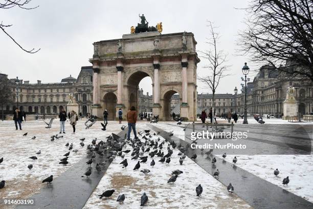 People walk around the Arc de Triomphe of the Carroussel du Louvre as snow falls in Paris on February 5, 2018. Much of France, including Paris was on...