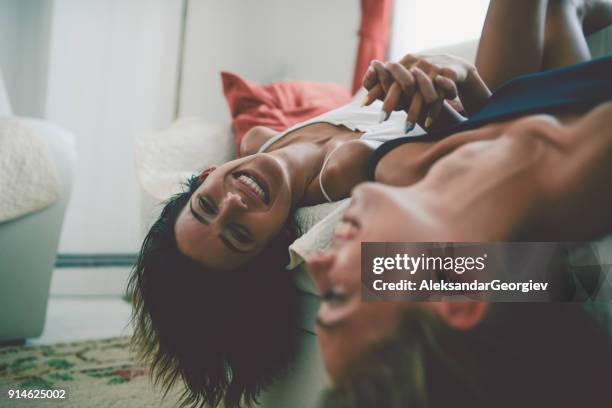 two laughing sensual females lying on sofa and holding hands upside down - lesbian couple stock pictures, royalty-free photos & images