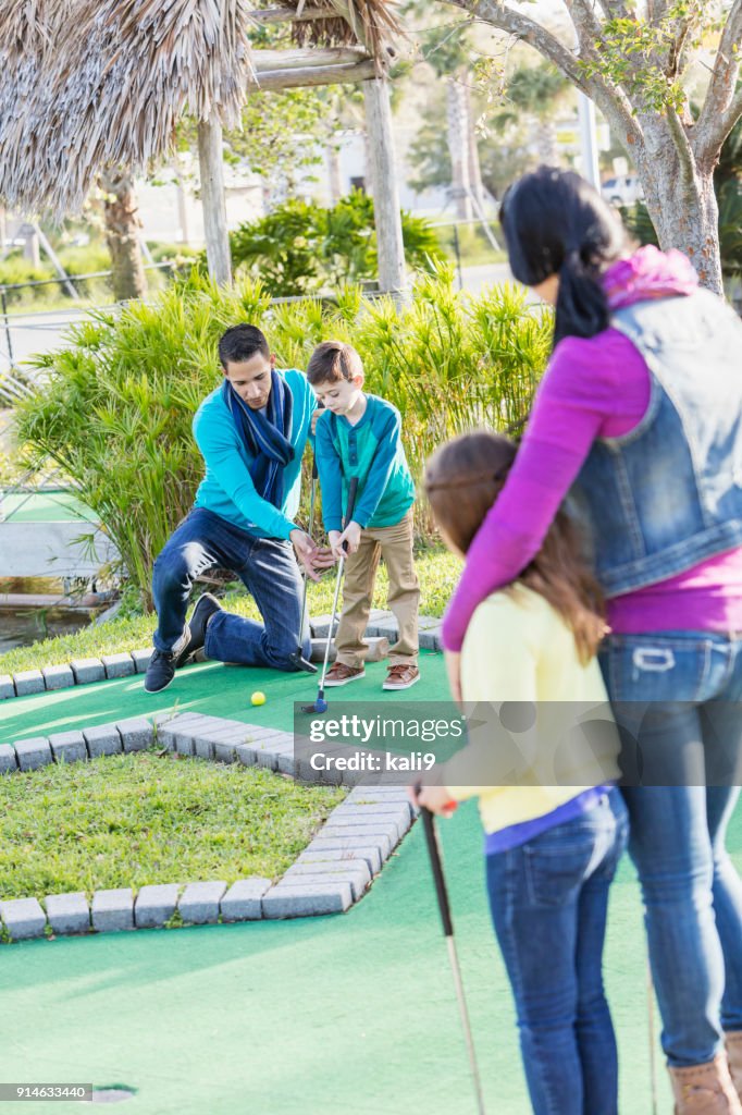 Familie spielt Minigolf, Papa hilft Sohn