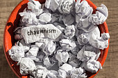 Crumpled paper written chauvism inside the trash can. Paper balls. Concept of old and abandoned idea or practice.