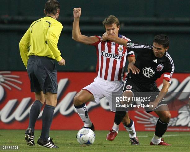 Jaime Moreno of D.C. United battles with Carey Talley of Chivas USA in front of referee Kevin Stott during an MLS match at RFK Stadium on October 3,...
