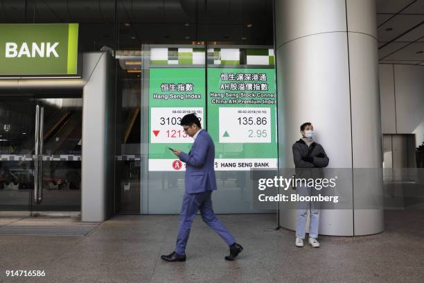 Pedestrian looks at his smartphone as he walks past an electronic screen displaying the Hang Seng Index and the Hang Seng Stock Connect China AH...