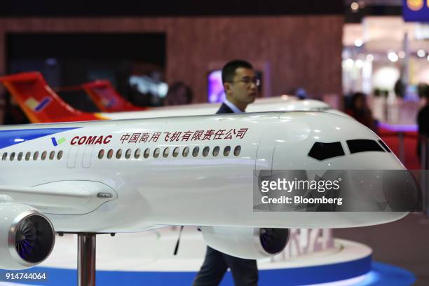 Visitor walks past a scale model of a Commercial Aircraft Corp. Of China Ltd. Aircraft at the Singapore Airshow held at the Changi Exhibition Centre...