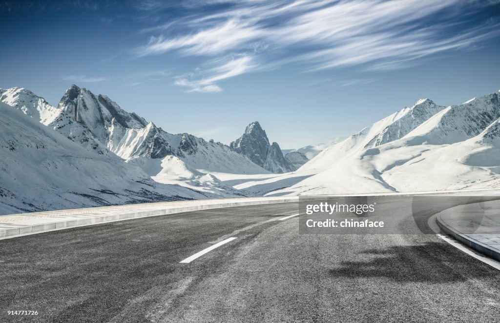 Empty asphalt road leading towards snow mountains