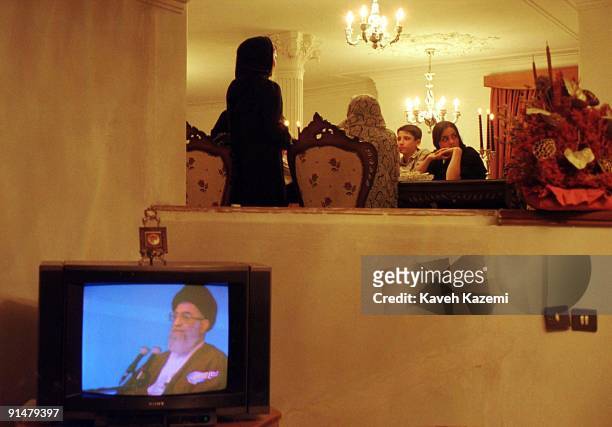 Family gather around the dinner table in the evening while the TV set is on in the foreground, with an image of Ayatollah Ali Khamenei on the screen,...