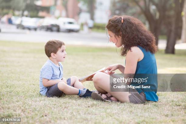 little boy reading book with his mother - moving down to seated position stock pictures, royalty-free photos & images