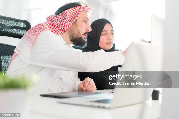 arabic business male and female working together on project - emirati guy using laptop stock-fotos und bilder