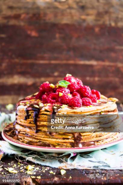 stack of wheat golden pancakes or pancake cake with freshly picked raspberry, chopped pistachios, chocolate sauce on a dessert plate, selective focus - freshers week stock pictures, royalty-free photos & images