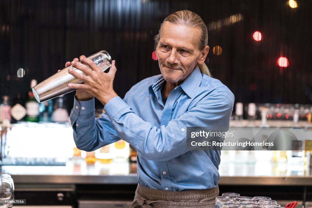 A bartender happily preparing a drink with a cocktail shaker