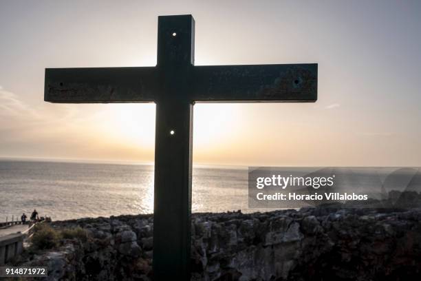 Cross covers the sun at sunset in mild winter weather at Boca do Inferno on January 30, 2018 in Cascais, Portugal. Mild and sunny winter weather is...