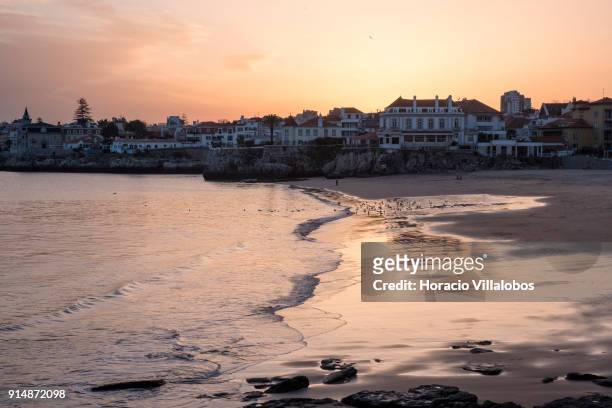 Tourists and seagulls at sunset enjoy mild winter weather at Praia da Duquesa on January 30, 2018 in Cascais, Portugal. Mild and sunny winter weather...
