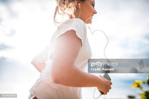young woman listening to music and jogging - hormone stock pictures, royalty-free photos & images