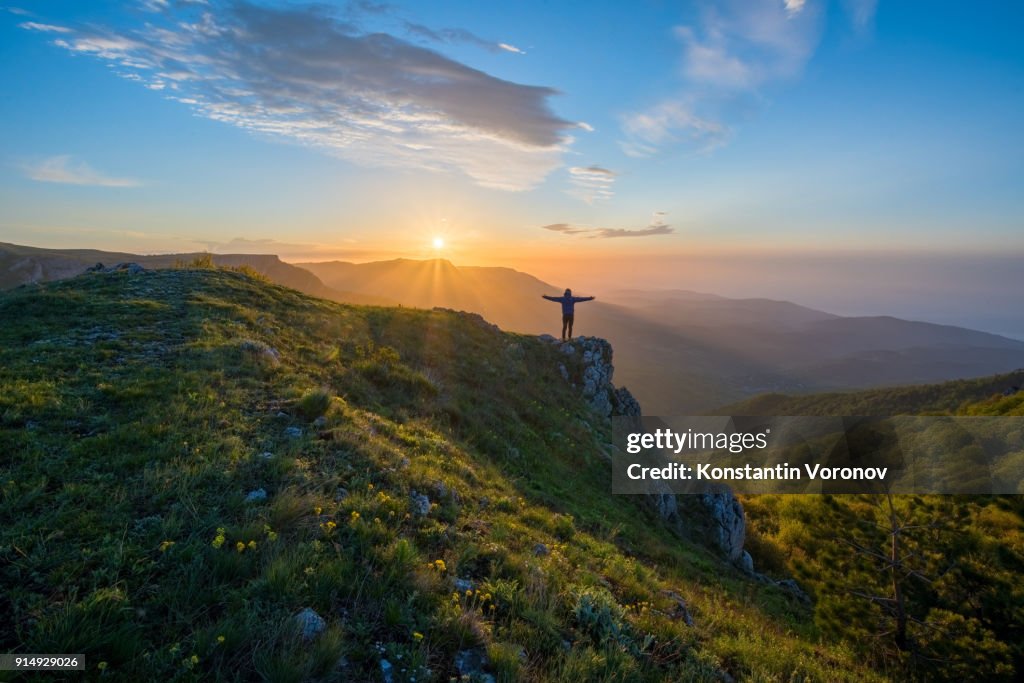 The traveler welcomes the sun at dawn in the highlands. Summer landscape with the sun. In the distance you can see the sea.