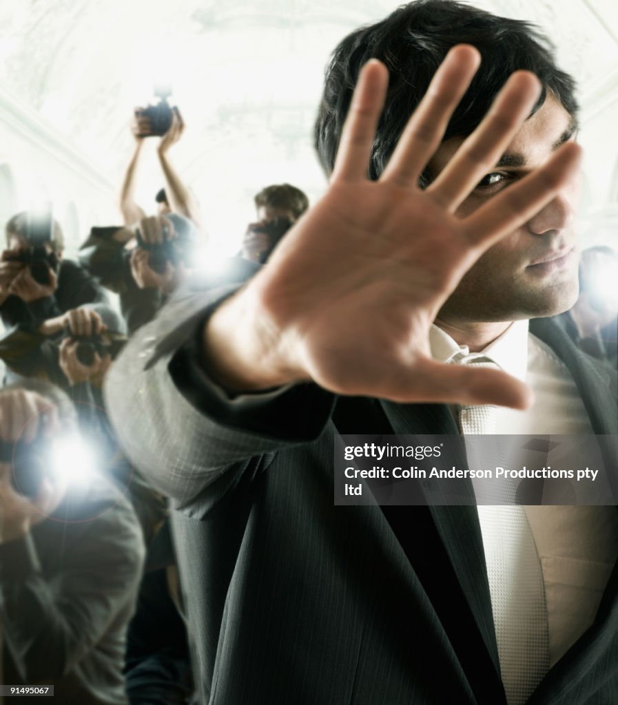Young male celebrity shielding face from photographers