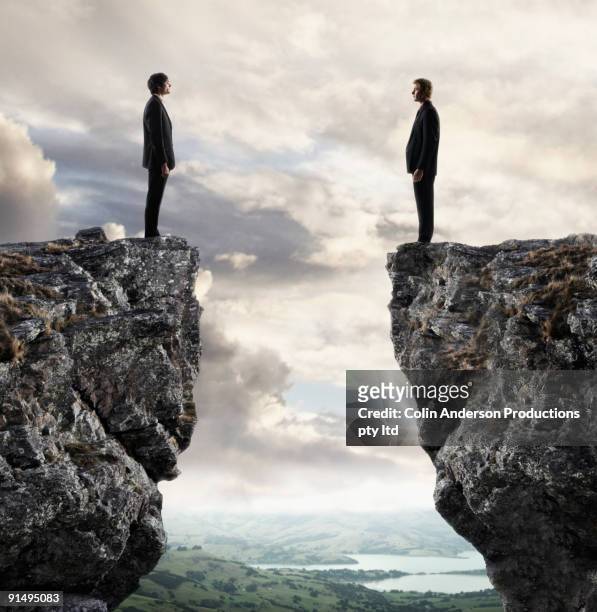 businessmen looking at each other across chasm - rivaliteit stockfoto's en -beelden