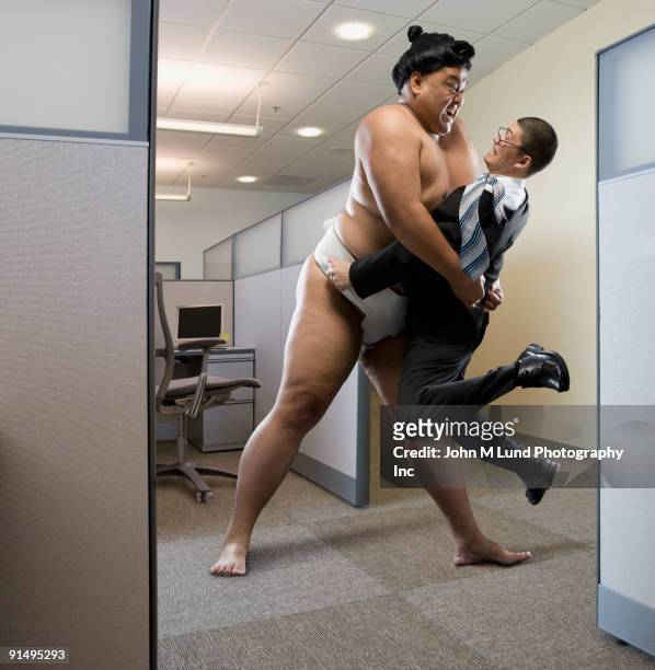 pacific islander sumo wrestler lifting businessman in office - sumo stock-fotos und bilder