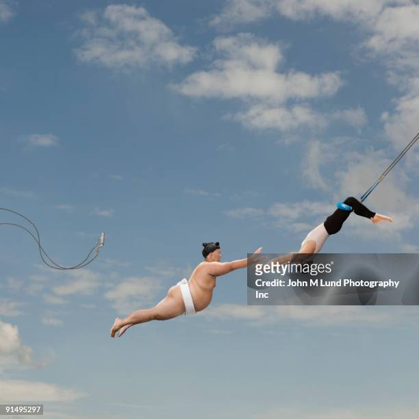pacific islander sumo wrestler reaching for trapeze artist - trapeze stock-fotos und bilder