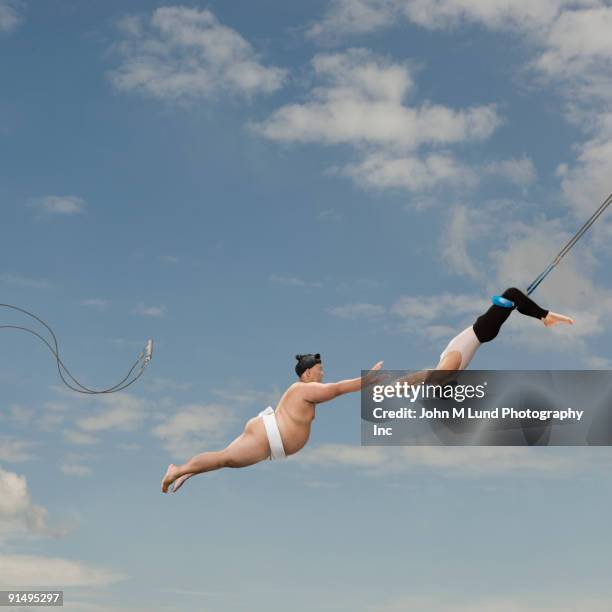pacific islander sumo wrestler reaching for trapeze artist - trapeze artist stock pictures, royalty-free photos & images