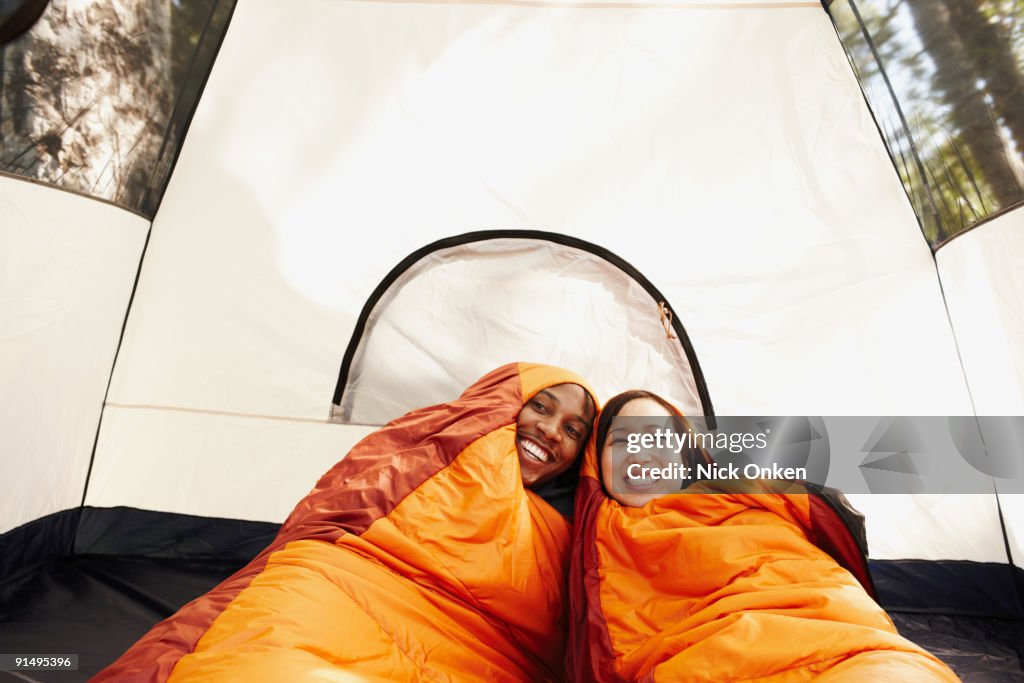 Multi-ethnic couple inside sleeping bags and tent