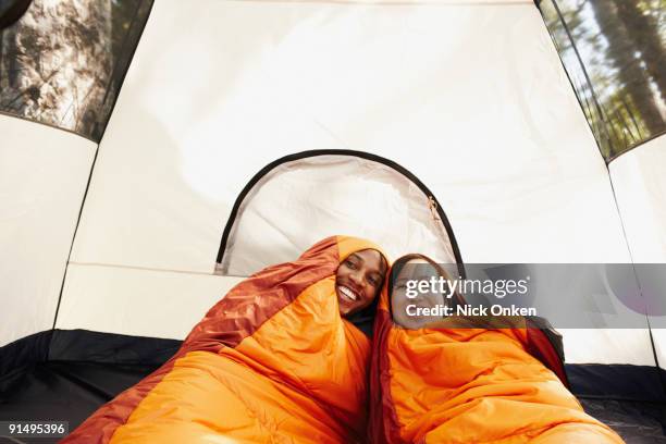 multi-ethnic couple inside sleeping bags and tent - sleeping bag stock pictures, royalty-free photos & images