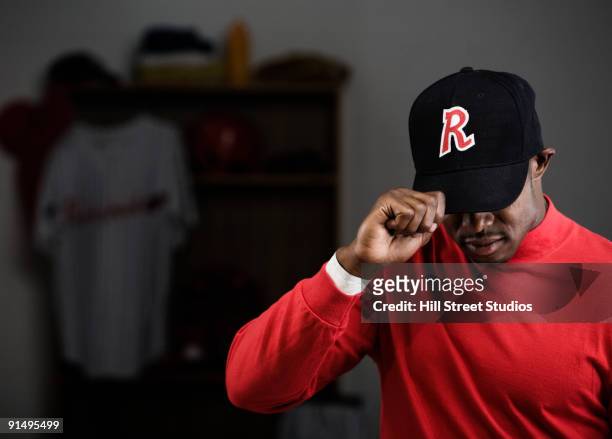 african baseball player adjusting cap in locker room - gorra de béisbol fotografías e imágenes de stock