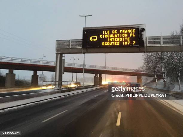 Vehicles travel through fresh snowfall under a traffic information sign - which reads that trucks are prohibited and advises to listen to local radio...