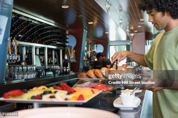 mixed race man choosing food from breakfast buffet - breakfast buffet stock pictures, royalty-free photos & images