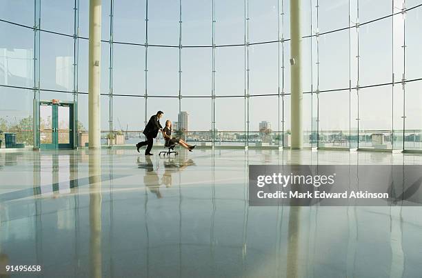 businessman pushing businesswoman in rolling desk chair - rollup photos et images de collection