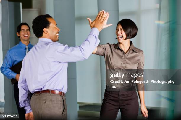 multi-ethnic co-workers high fiving in office - business high five stock pictures, royalty-free photos & images