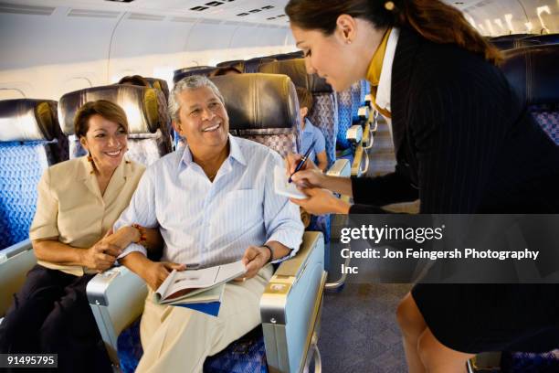 flight attendant helping couple on airplane - arm in arm stock pictures, royalty-free photos & images