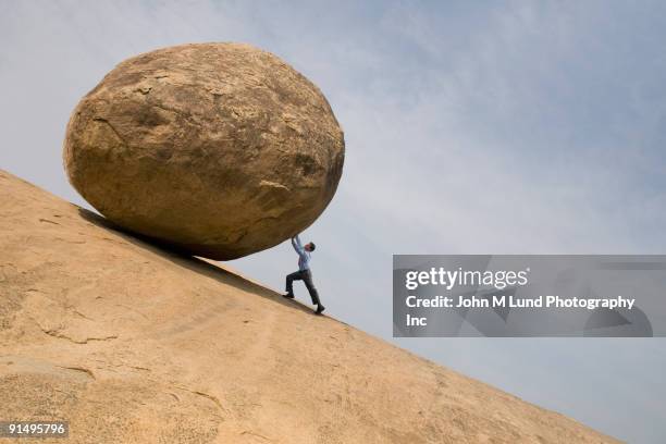 businessman pushing large rock uphill - push stock pictures, royalty-free photos & images