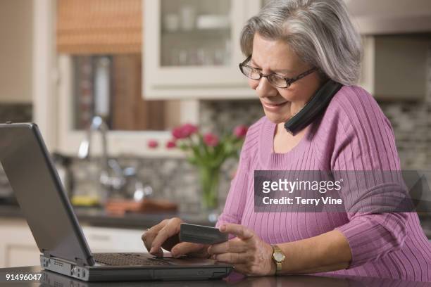 senior hispanic woman shopping online with credit card - landline phone home stock pictures, royalty-free photos & images