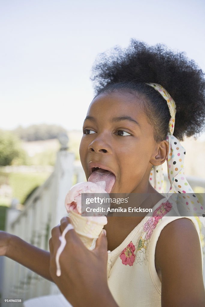 Mixed race girl licking melting ice cream cone