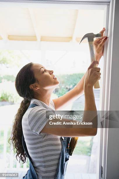 mixed race woman hammering nail in doorway - hamer stockfoto's en -beelden