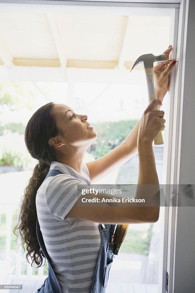 Mixed race woman hammering nail in doorway