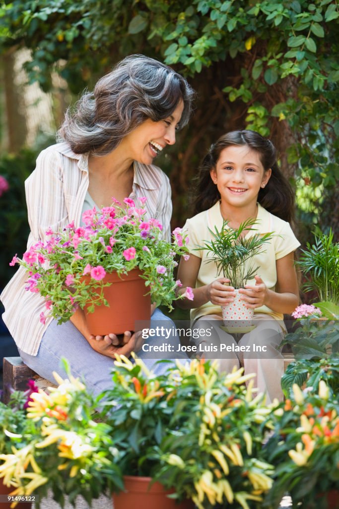 Hispanic grandmother and granddaughter holding plants in garden