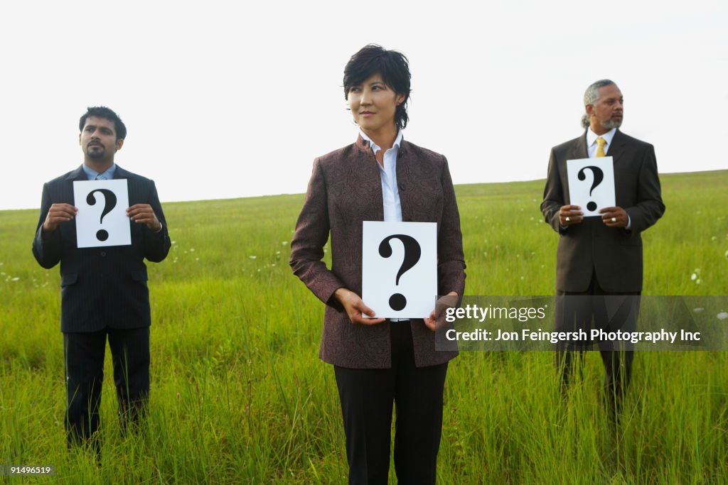 Businesspeople holding question marks in field