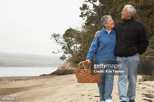 senior asian couple walking on beach with picnic basket - asian couple walking stock pictures, royalty-free photos & images