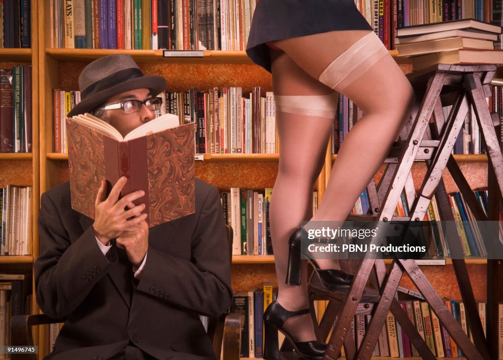 Man looking up woman's skirt in library