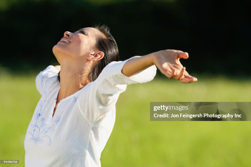 Asian woman standing in meadow with arms outstretched