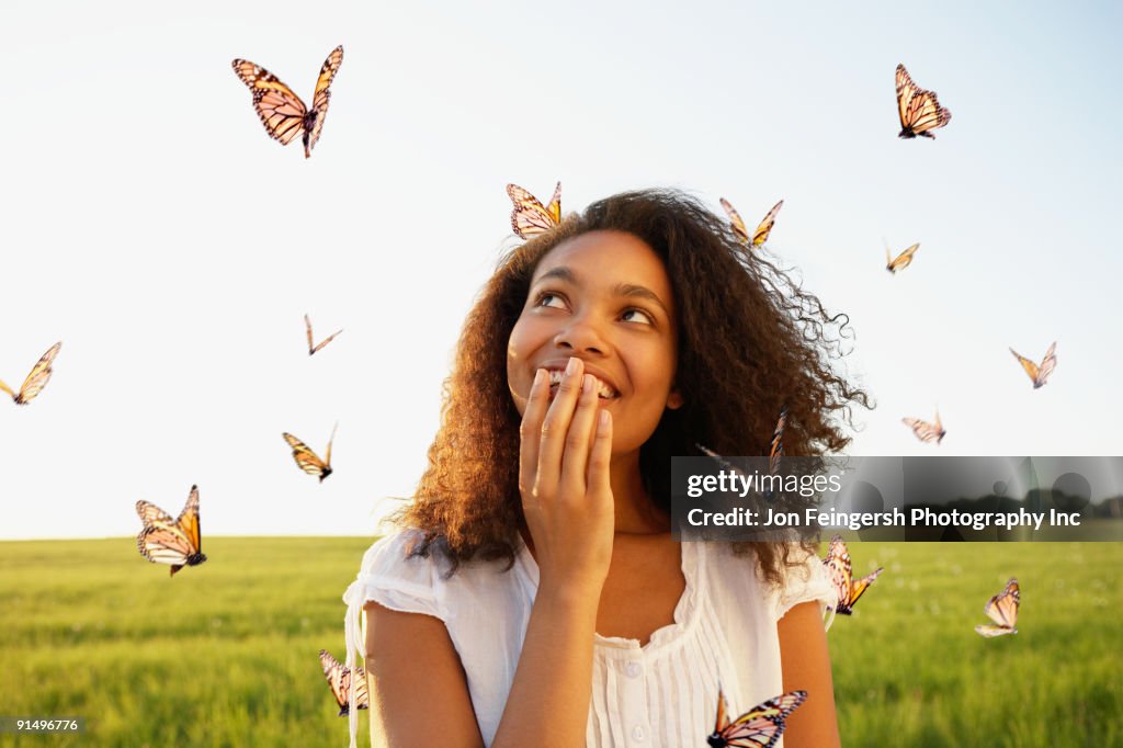 African woman standing among butterflies in meadow