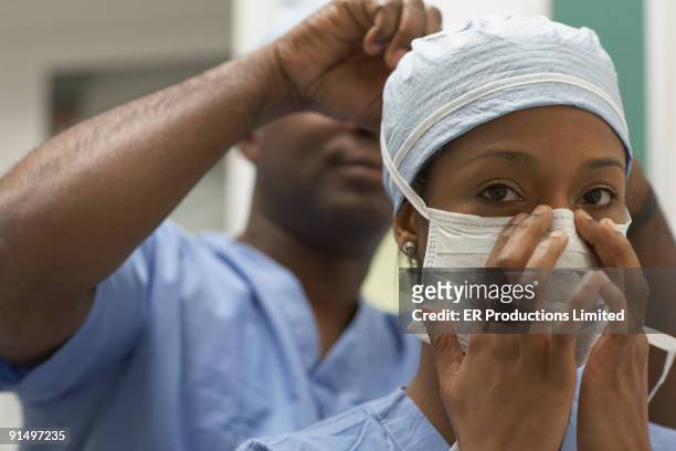 african american medical professional tying coworker's surgical mask - female surgeon mask - fotografias e filmes do acervo
