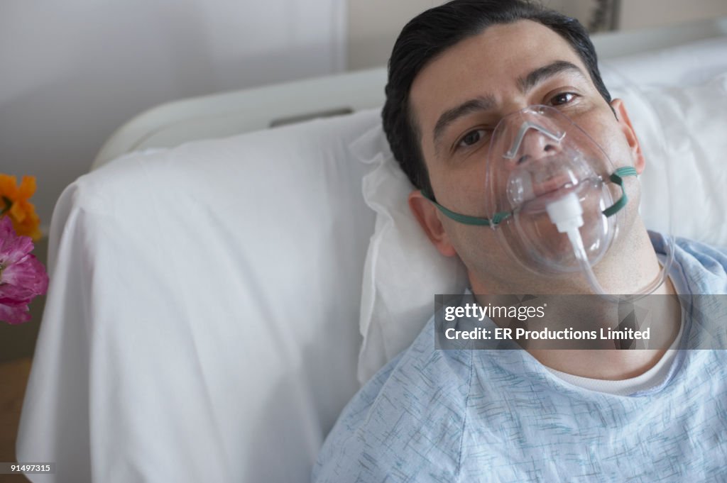 Hispanic man wearing oxygen mask in hospital