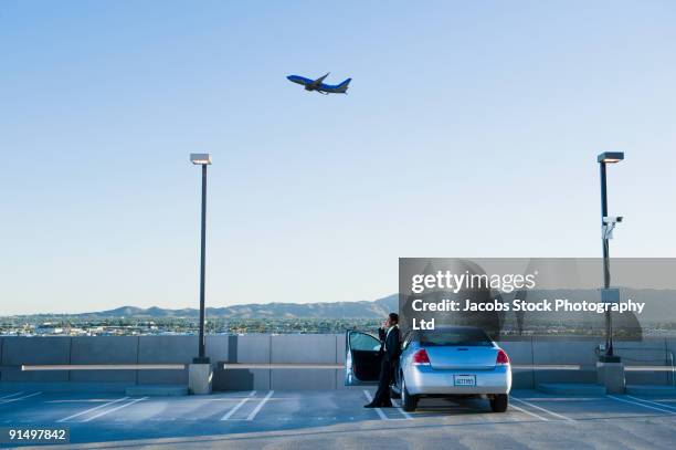 african businessman standing by car at airport - parking foto e immagini stock