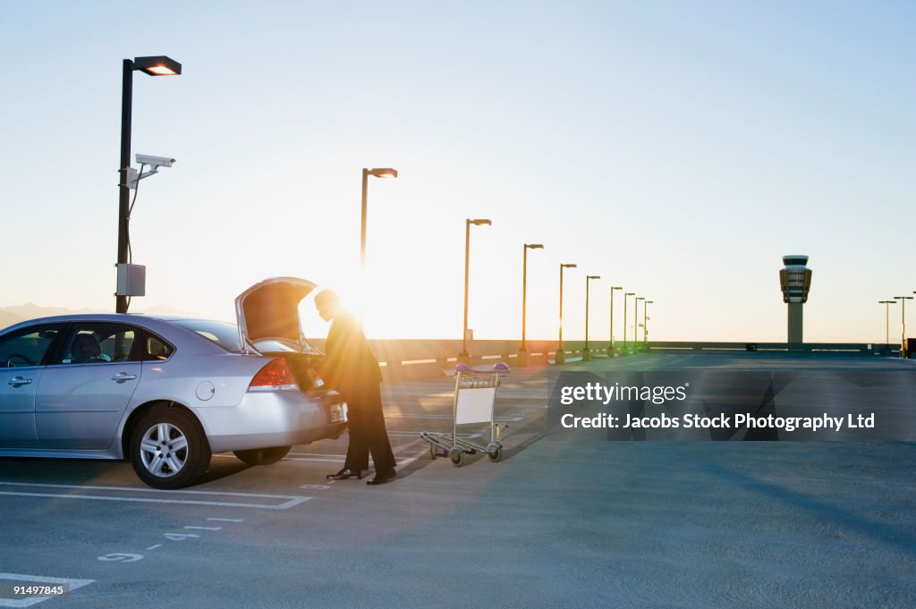 African businessman loading luggage into car