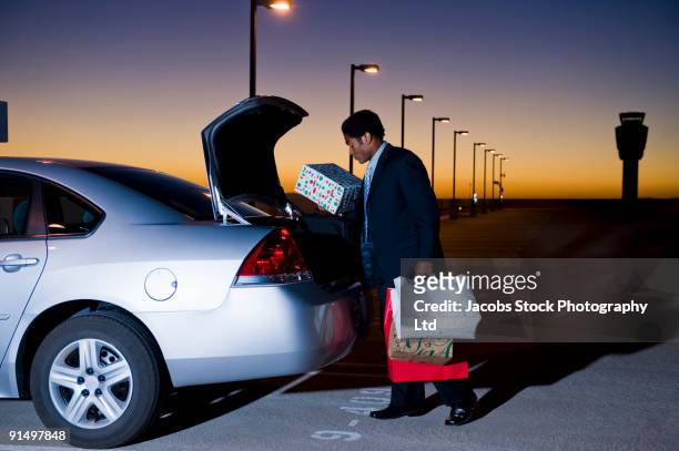 african businessman loading packages into car in parking lot - shopping bags car boot stock pictures, royalty-free photos & images