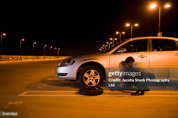 african businessman changing flat tire in parking lot - flat tyre stock pictures, royalty-free photos & images