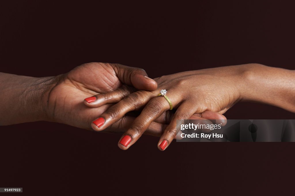 African woman with engagement ring holding fiancee's hand