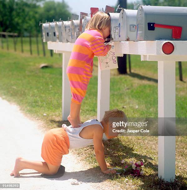 girl standing on brother's back and peering into mailbox - kins fotografías e imágenes de stock