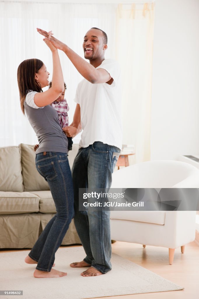 African couple and baby dancing in living room
